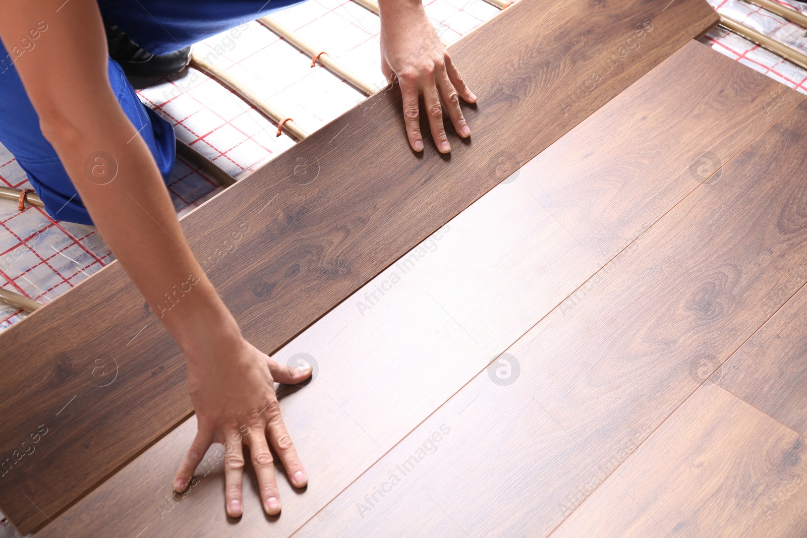 Photo of Worker installing new wooden laminate over underfloor heating system, closeup