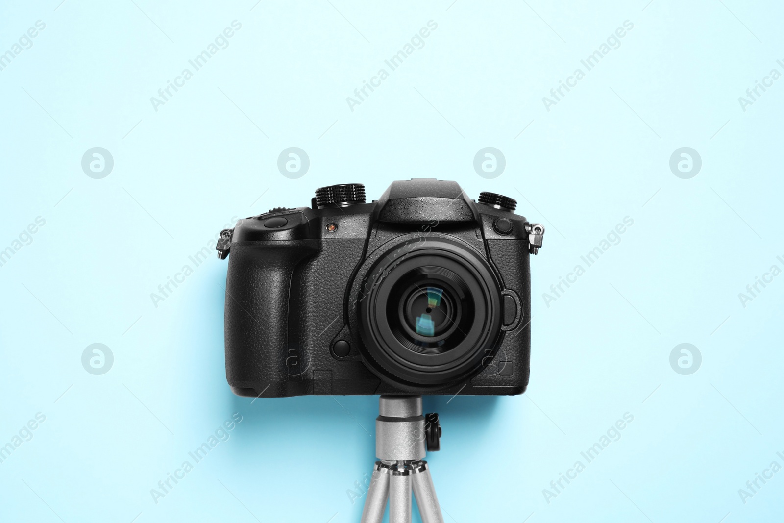 Photo of Modern camera with mini tripod on light blue background, flat lay. Video production equipment