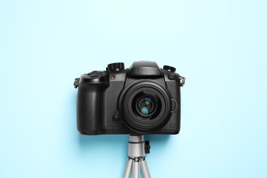 Photo of Modern camera with mini tripod on light blue background, flat lay. Video production equipment