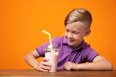 Photo of Little boy with cup of milk shake at table on color background