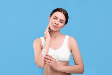 Photo of Beautiful woman with smear of body cream on her arm against light blue background