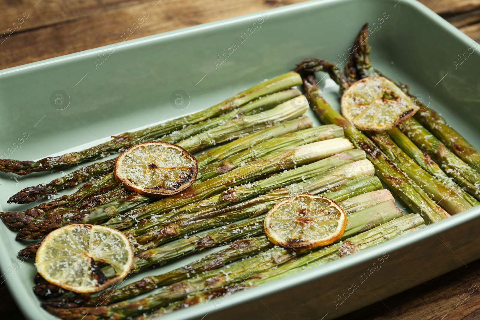 Photo of Oven baked asparagus with lemon slices in ceramic dish on table, closeup