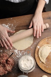 Woman rolling dough for chebureki on wooden table, top view