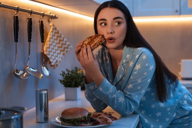 Photo of Young woman eating sandwich in kitchen at night. Bad habit