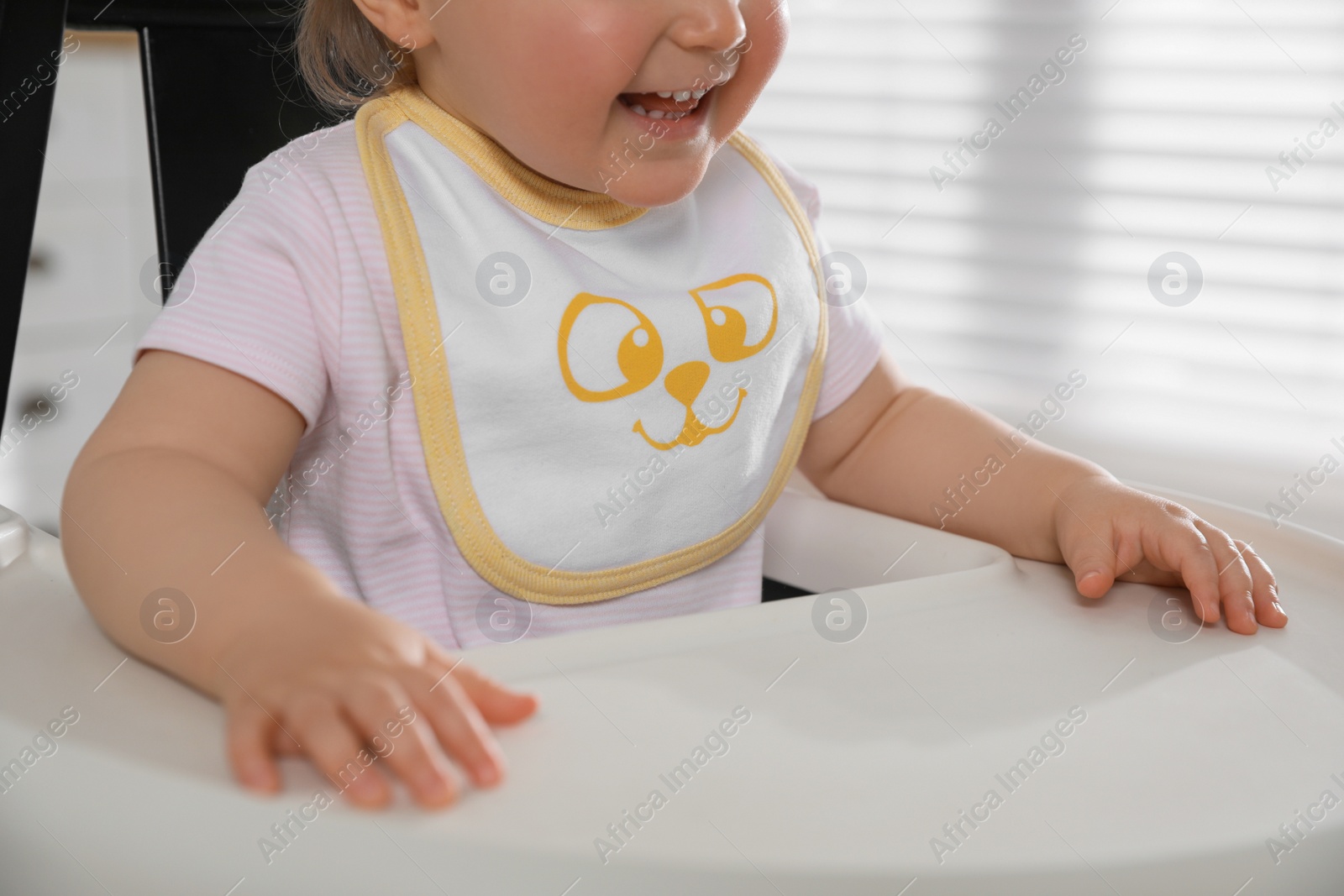 Photo of Cute little baby wearing bib in highchair at home, closeup