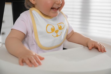 Photo of Cute little baby wearing bib in highchair at home, closeup