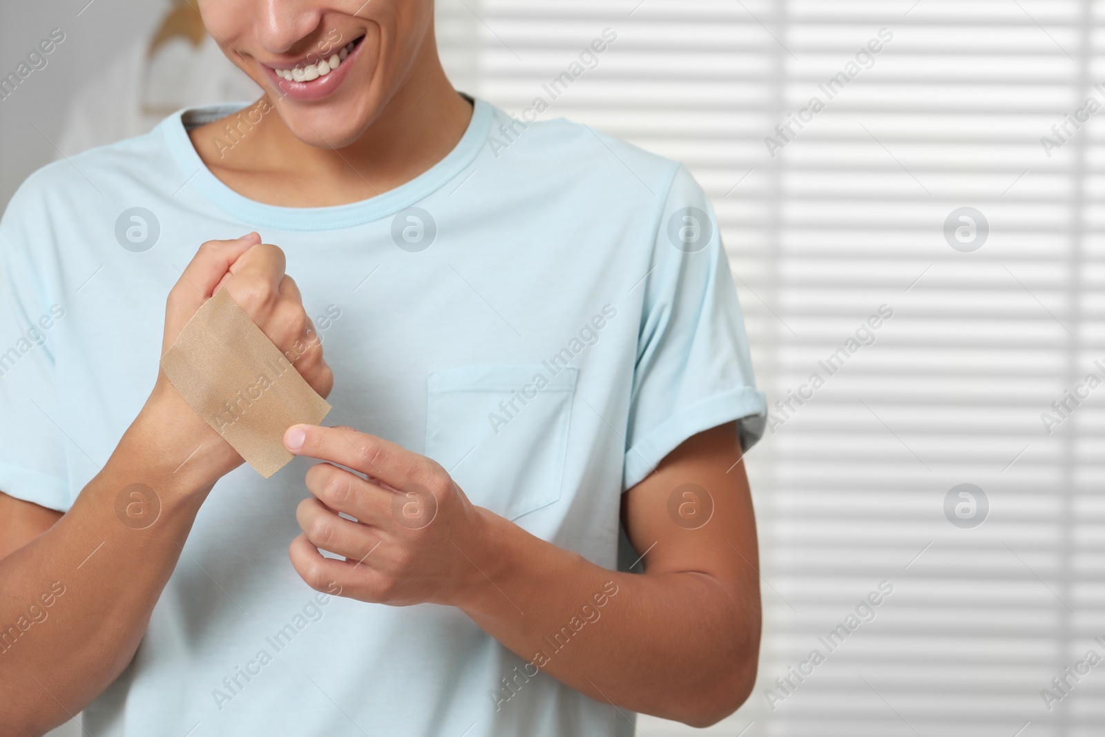 Photo of Man putting sticking plaster onto hand indoors, closeup