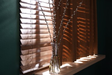 Glass vase with pussy willow tree branches on wooden windowsill