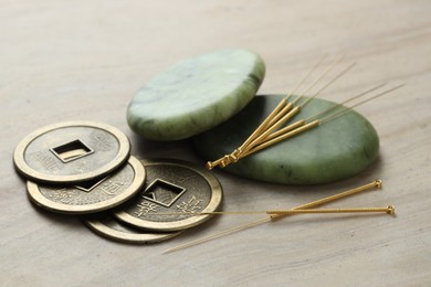 Acupuncture needles, stones and Chinese coins on beige marble table, closeup