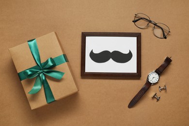 Photo of Gift box, frame with paper mustache and men accessories on brown background, flat lay. Father's day celebration