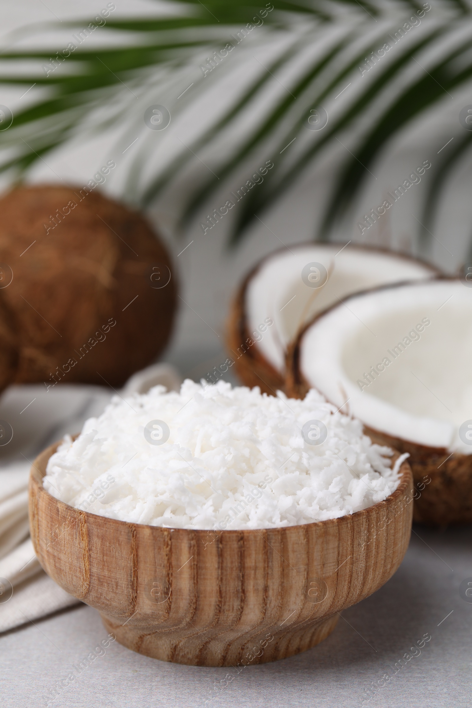 Photo of Coconut flakes in bowl and nuts on light grey table