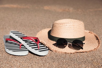 Photo of Striped flip flops, straw hat and sunglasses on sandy seashore