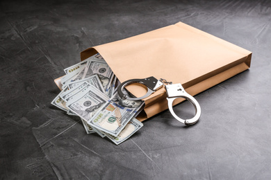 Photo of Envelope with dollar bills and handcuffs on grey stone table. Bribe concept