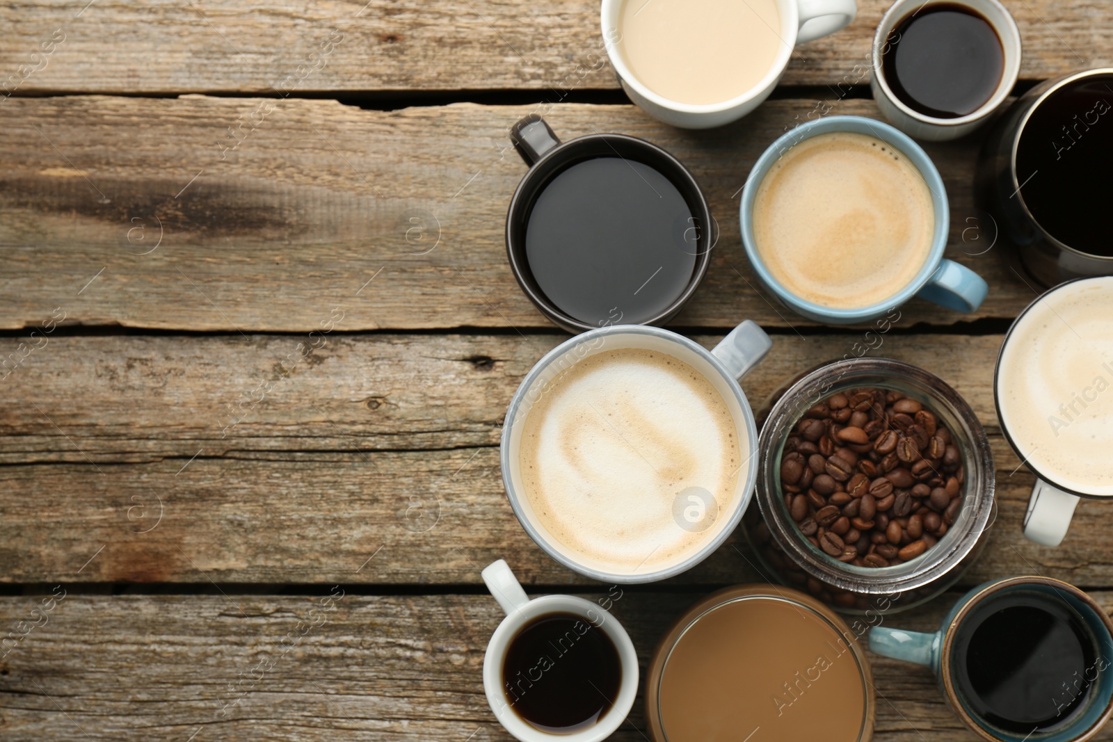Photo of Different coffee drinks in cups and beans on wooden table, flat lay. Space for text