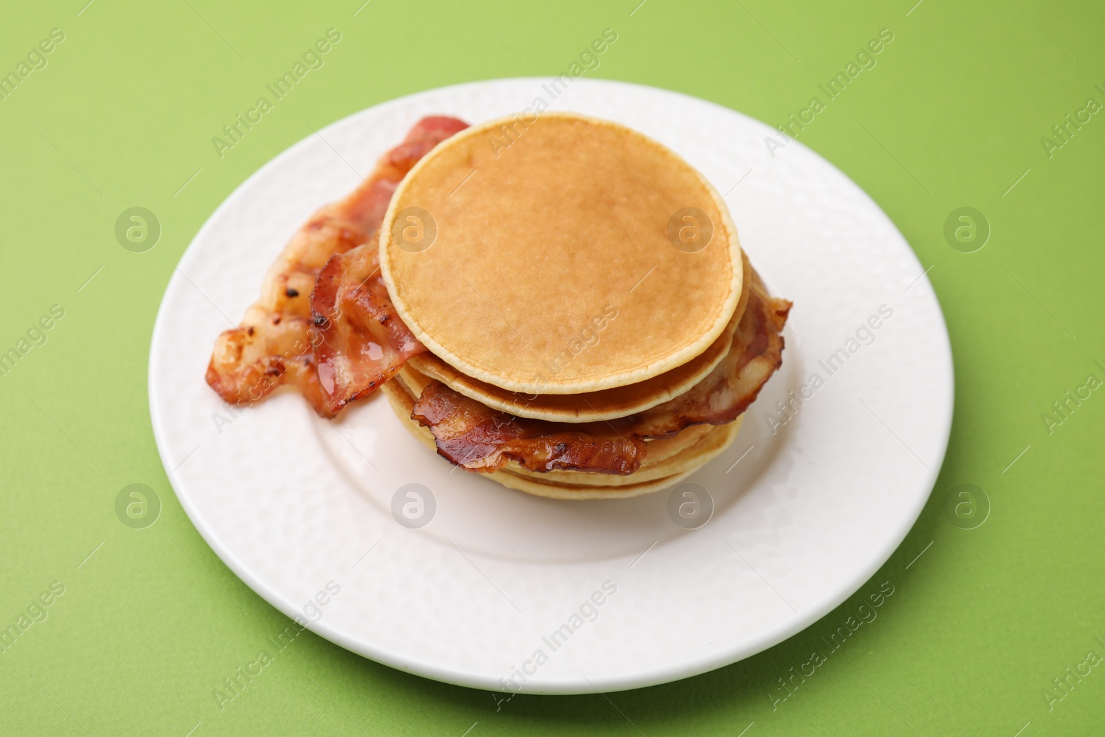 Photo of Delicious pancakes with bacon on green table, closeup