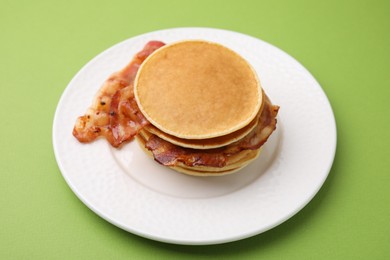 Delicious pancakes with bacon on green table, closeup