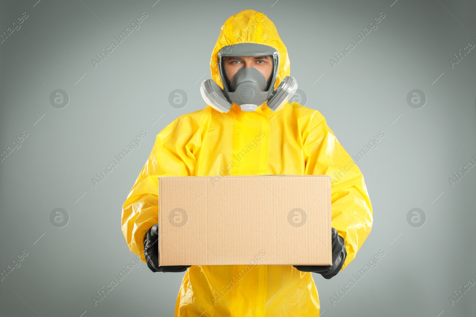 Photo of Man wearing chemical protective suit with cardboard box on light grey background. Prevention of virus spread