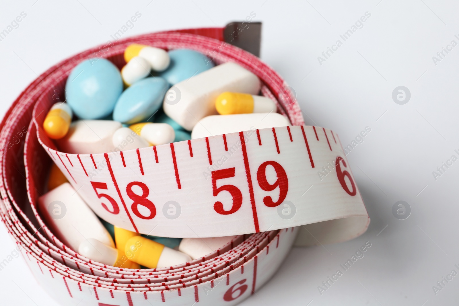 Photo of Weight loss pills and measuring tape on white background