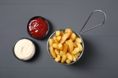 Tasty French fries, ketchup and mayonnaise on grey table, flat lay