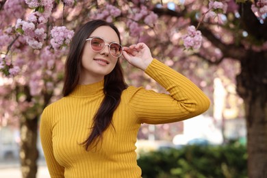 Photo of Beautiful woman in sunglasses near blossoming tree on spring day