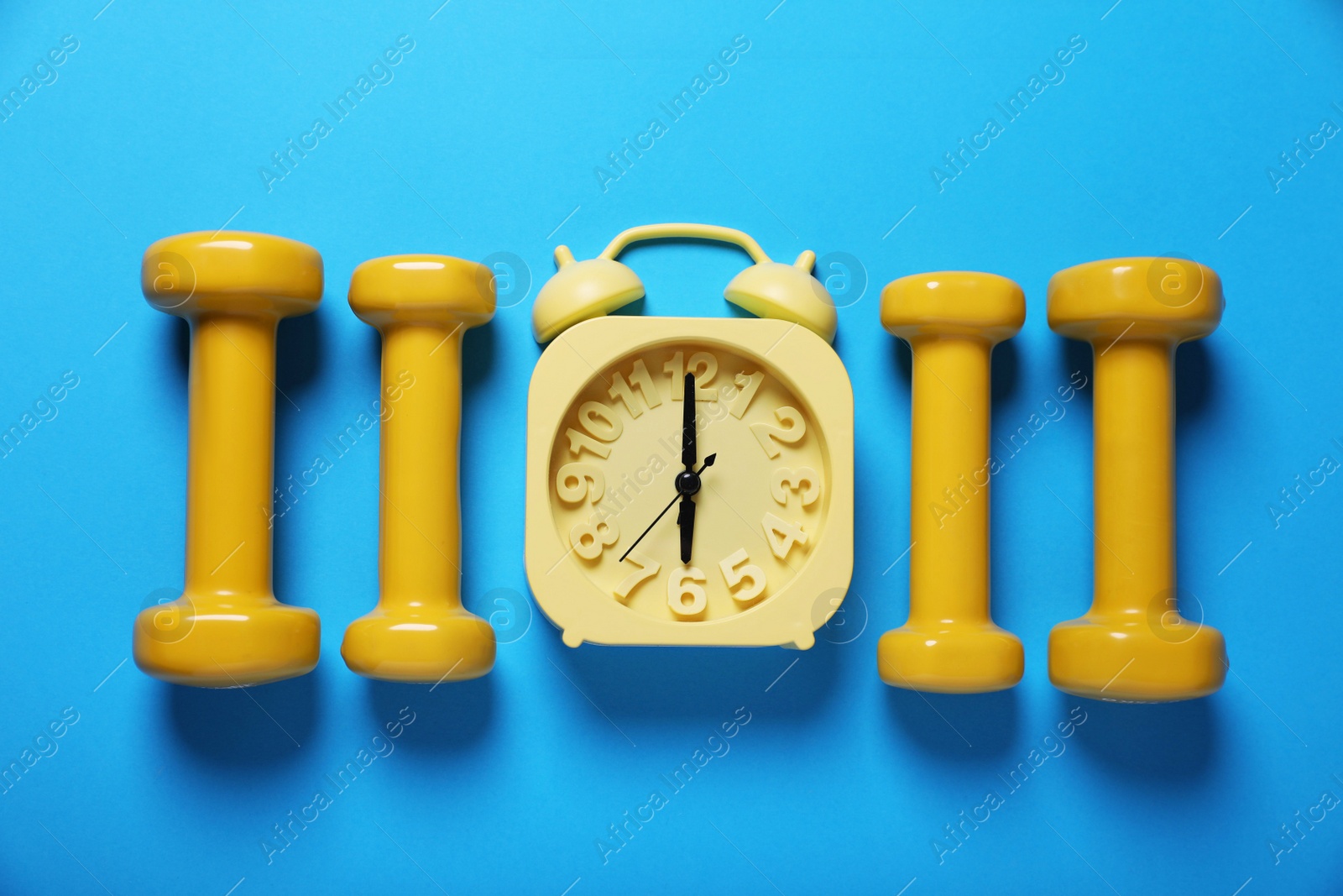 Photo of Yellow alarm clock and dumbbells on light blue background, flat lay. Morning exercise