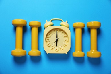 Photo of Yellow alarm clock and dumbbells on light blue background, flat lay. Morning exercise