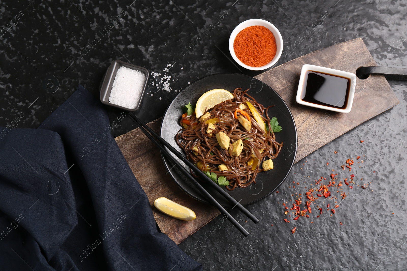 Photo of Stir-fry. Tasty noodles with vegetables and meat served on dark textured table, flat lay