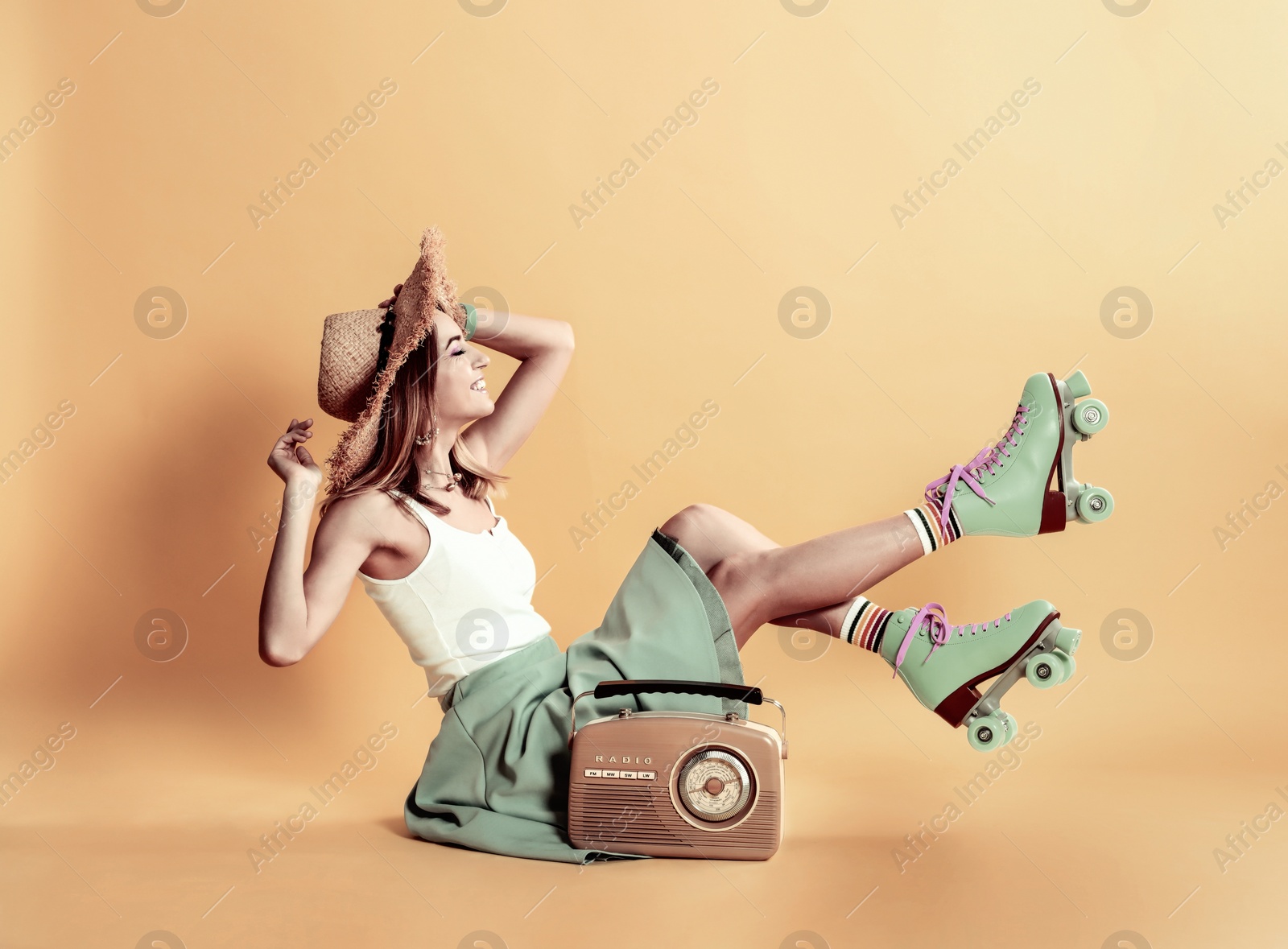 Image of Young woman with roller skates and retro radio on orange background