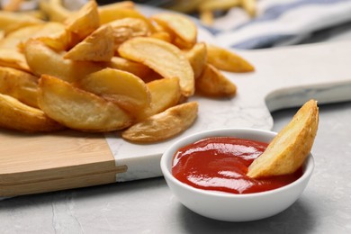 Photo of Delicious baked potato wedges and ketchup in bowl on light gray table, closeup