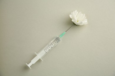 Photo of Medical syringe and beautiful chrysanthemum flower on grey background, top view