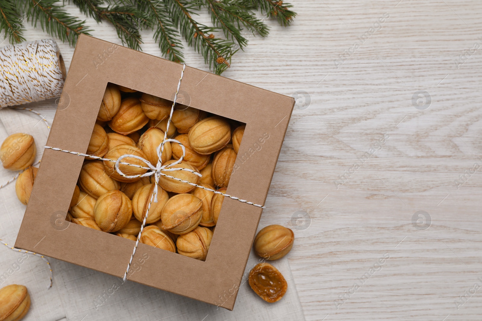 Photo of Delicious nut shaped cookies with boiled condensed milk in box and fir branch on white wooden table, flat lay. Space for text