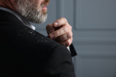Bearded man brushing dandruff off his jacket on grey background, closeup. Space for text
