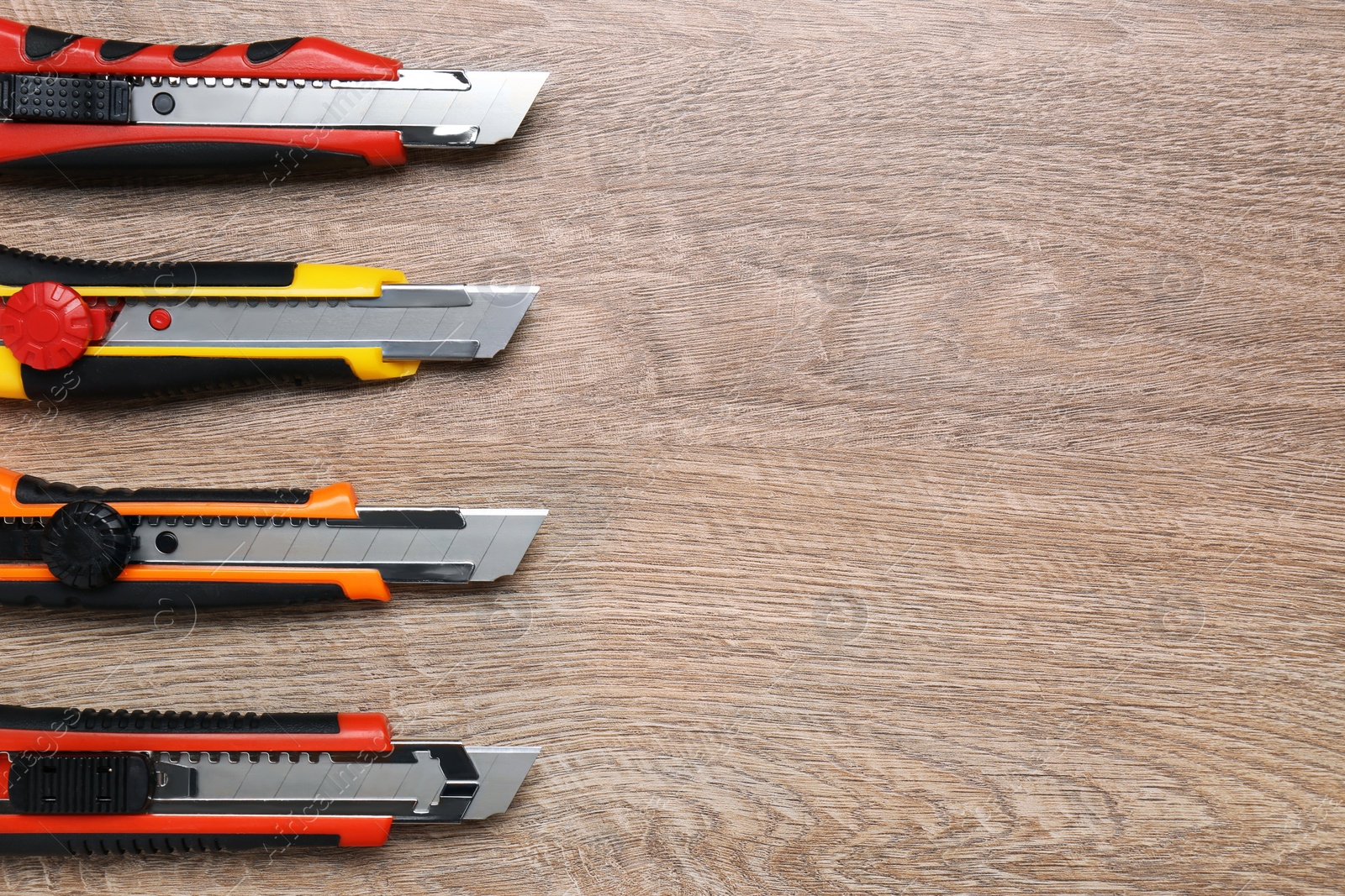 Photo of Many different utility knives on wooden table, flat lay. Space for text