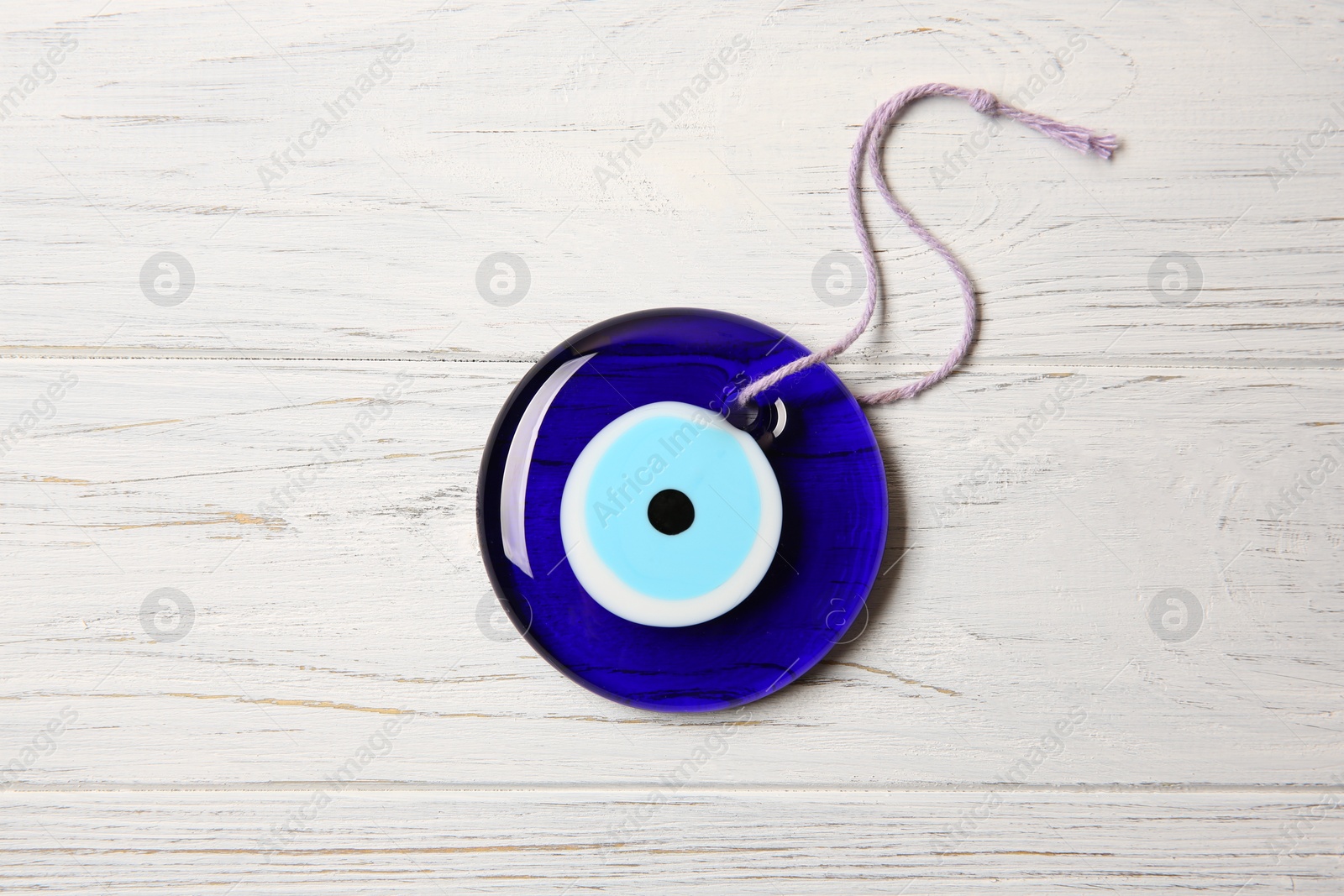 Photo of Evil eye amulet on white wooden table, top view