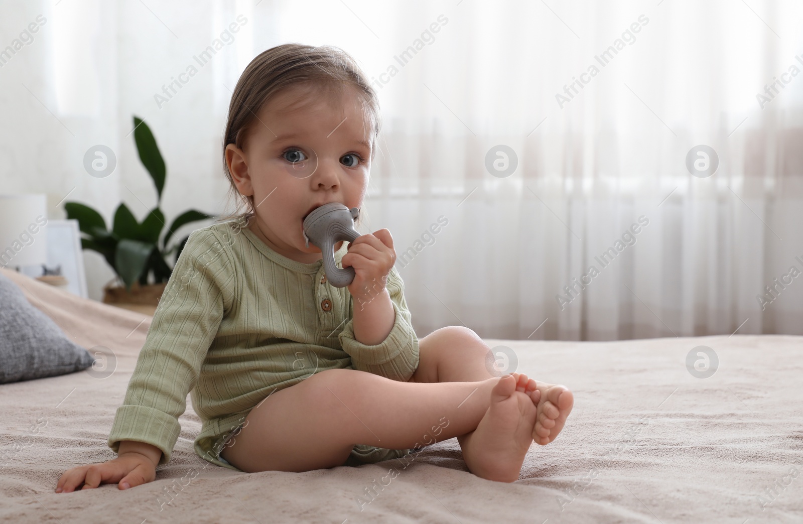Photo of Cute baby girl with nibbler on bed at home. Space for text