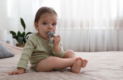 Cute baby girl with nibbler on bed at home. Space for text