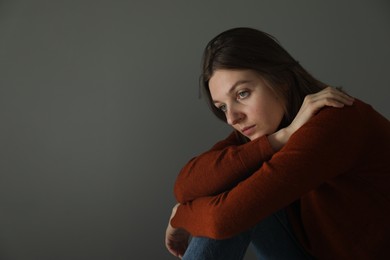 Photo of Sad young woman near grey wall indoors, space for text