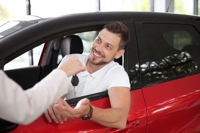 Photo of Female salesperson giving car key to man in auto dealership
