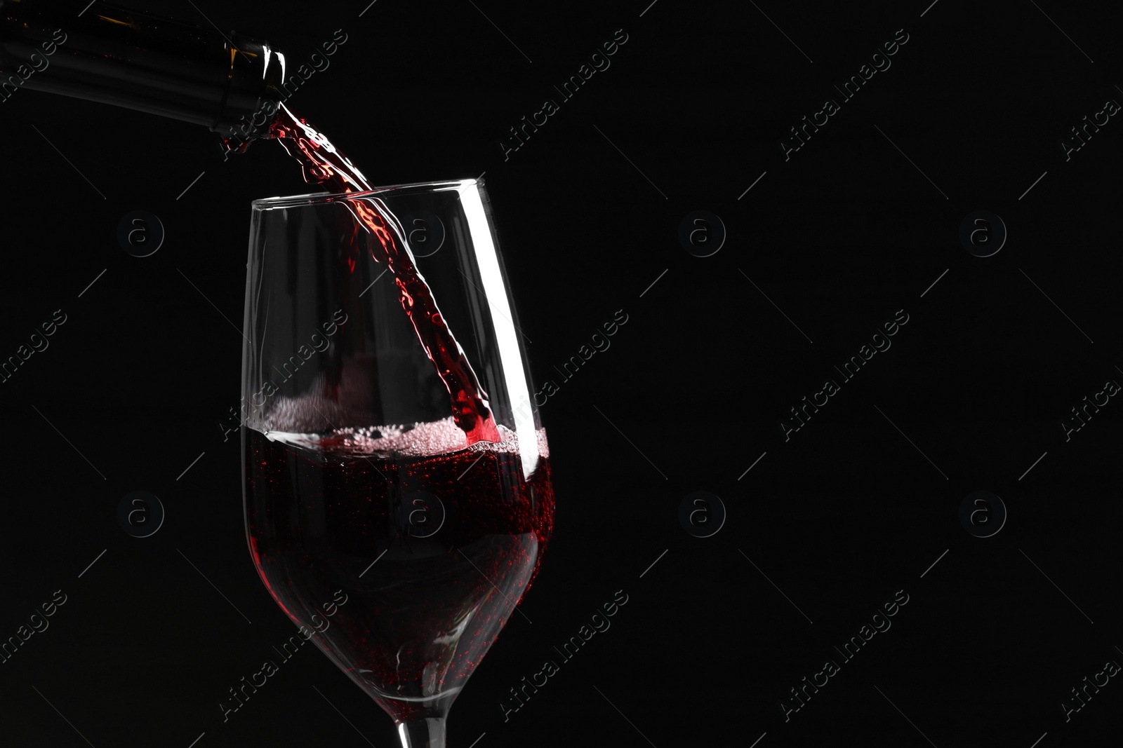 Photo of Pouring red wine into glass against black background, closeup. Space for text