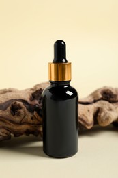 Bottle with cosmetic oil and wooden snag on beige background, closeup