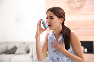 Young woman with asthma inhaler in light room