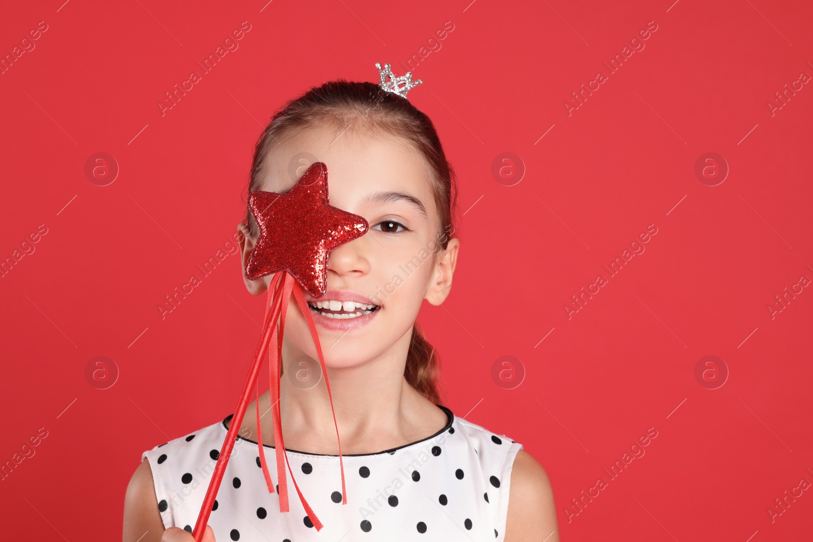 Photo of Cute girl with small crown and magic wand on red background. Little princess