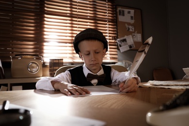Photo of Cute little detective writing with feather at table in office