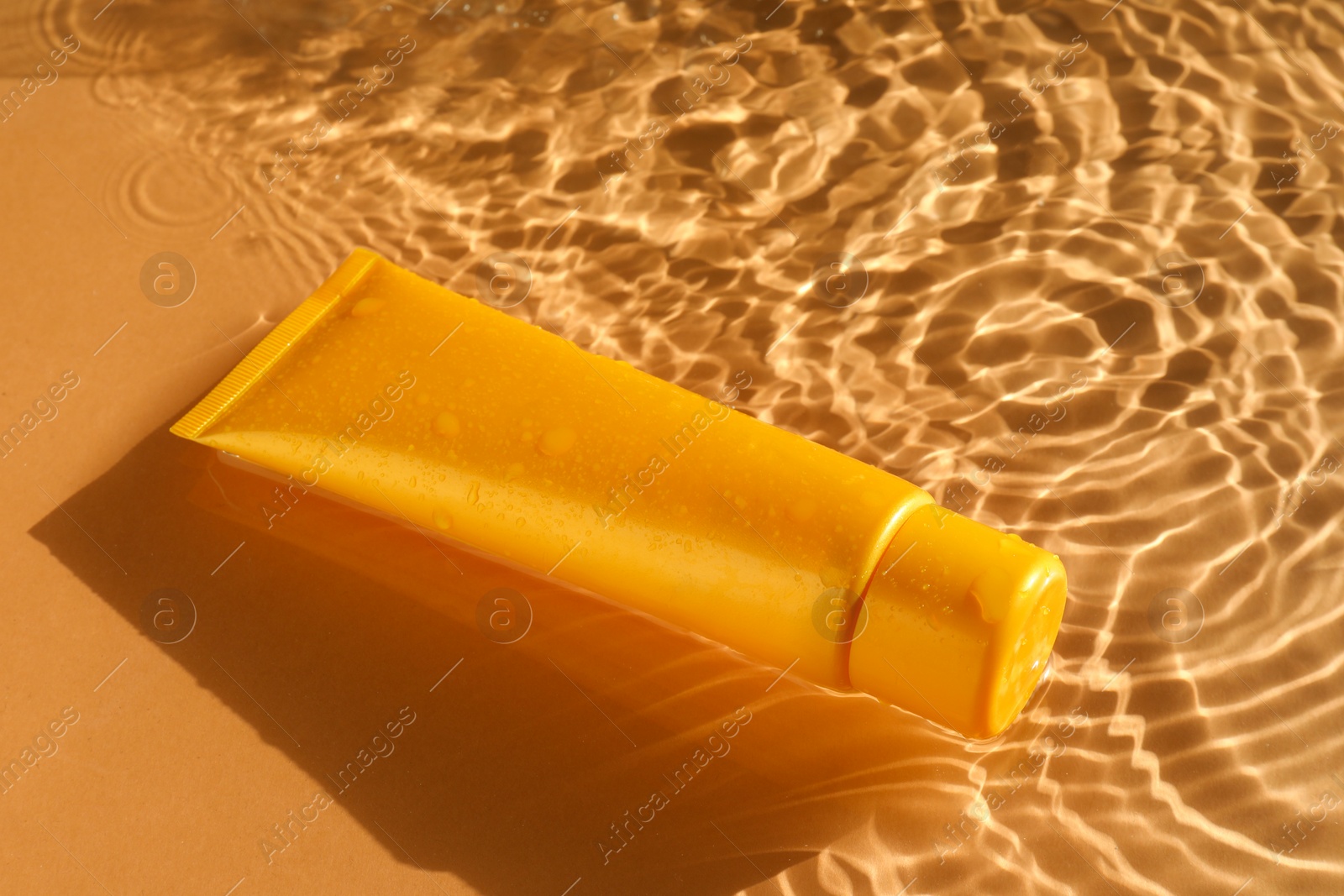 Photo of Tube with moisturizing cream in water on orange background