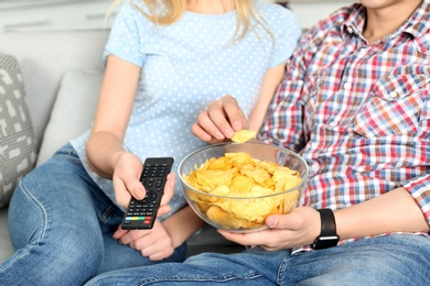 Photo of Young couple eating chips while watching TV, closeup view
