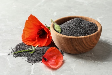 Wooden bowl of poppy seeds and flower on grey table