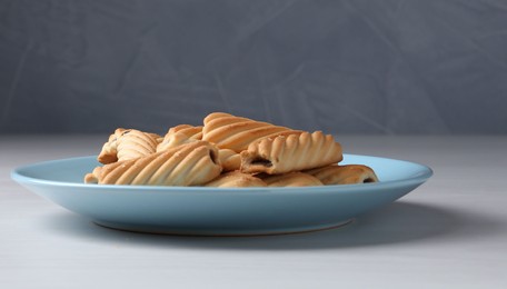 Photo of Woman with sieve sprinkling powdered sugar onto cookies at white wooden table, closeup