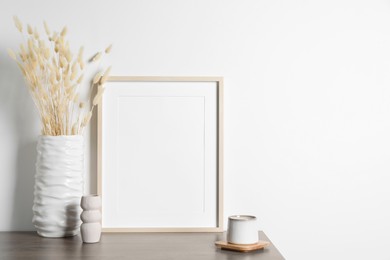 Empty photo frame, cup and vase with dry decorative spikes on wooden table. Mockup for design