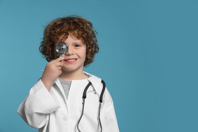 Little boy in medical uniform with stethoscope on light blue background. Space for text
