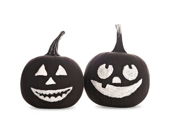 Photo of Black pumpkins with scary drawn faces on white background. Halloween celebration